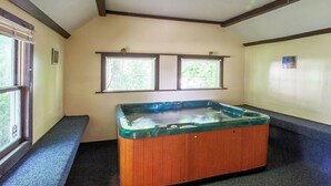 Un jacuzzi en una habitación con techo inclinado, dos ventanas con persianas y suelo alfombrado.