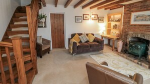 A cozy living room with a wooden staircase, a brown leather sofa, a wooden coffee table, and a brick fireplace. - Manor Cottage (Scarborough)