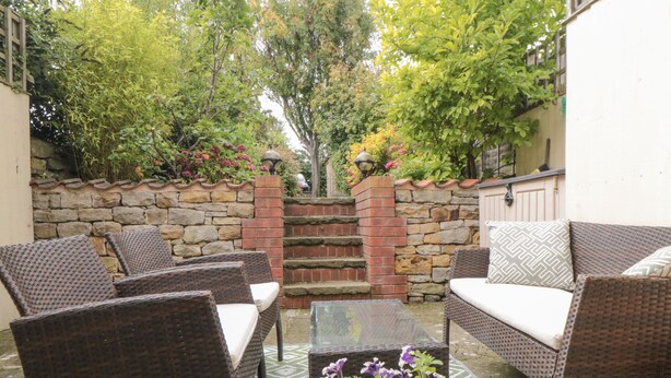 A patio with wicker furniture, a stone wall, and a variety of plants. - Manor Cottage (Scarborough)