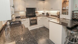 A modern kitchen with white cabinetry, a granite countertop, and a built-in oven. - Manor Cottage (Scarborough)