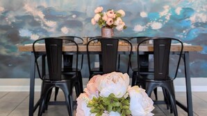 Une table à manger avec des chaises, un vase rempli de fleurs et un mur à motifs en arrière-plan.