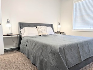 A bedroom with a bed, two bedside tables, a nightstand, a lamp, and a window with blinds. - Alabama Daydreaming 3BD/2.5 bath *5 min to base*pool (Enterprise)