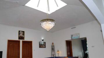 A spacious room with a pool table, wooden doors, a chandelier, and a large skylight.