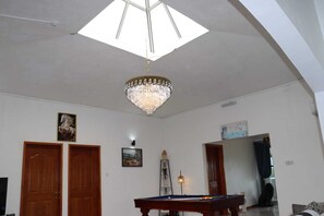 Une pièce spacieuse équipée d’une table de billard, de portes en bois, d’un lustre et d’une grande verrière.