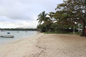 Une plage avec des bateaux, des palmiers et un bâtiment en arrière-plan.