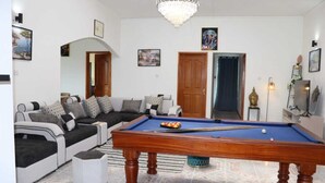 Un salon comprenant une table de billard, un canapé, un lustre et une statue de Bouddha.