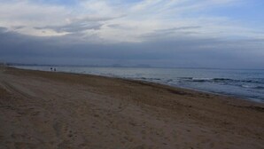 A beach with a sandy shore and a view of the ocean under a cloudy sky. - Hotel Doña Isabel (Elche)
