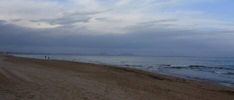 Une plage avec un rivage sablonneux et une vue sur l’océan, sous un ciel nuageux.