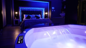 A modern bedroom with a large bed, a built-in headboard, and a jacuzzi tub. - HOTEL ANGIOINO & SPA (Naples)
