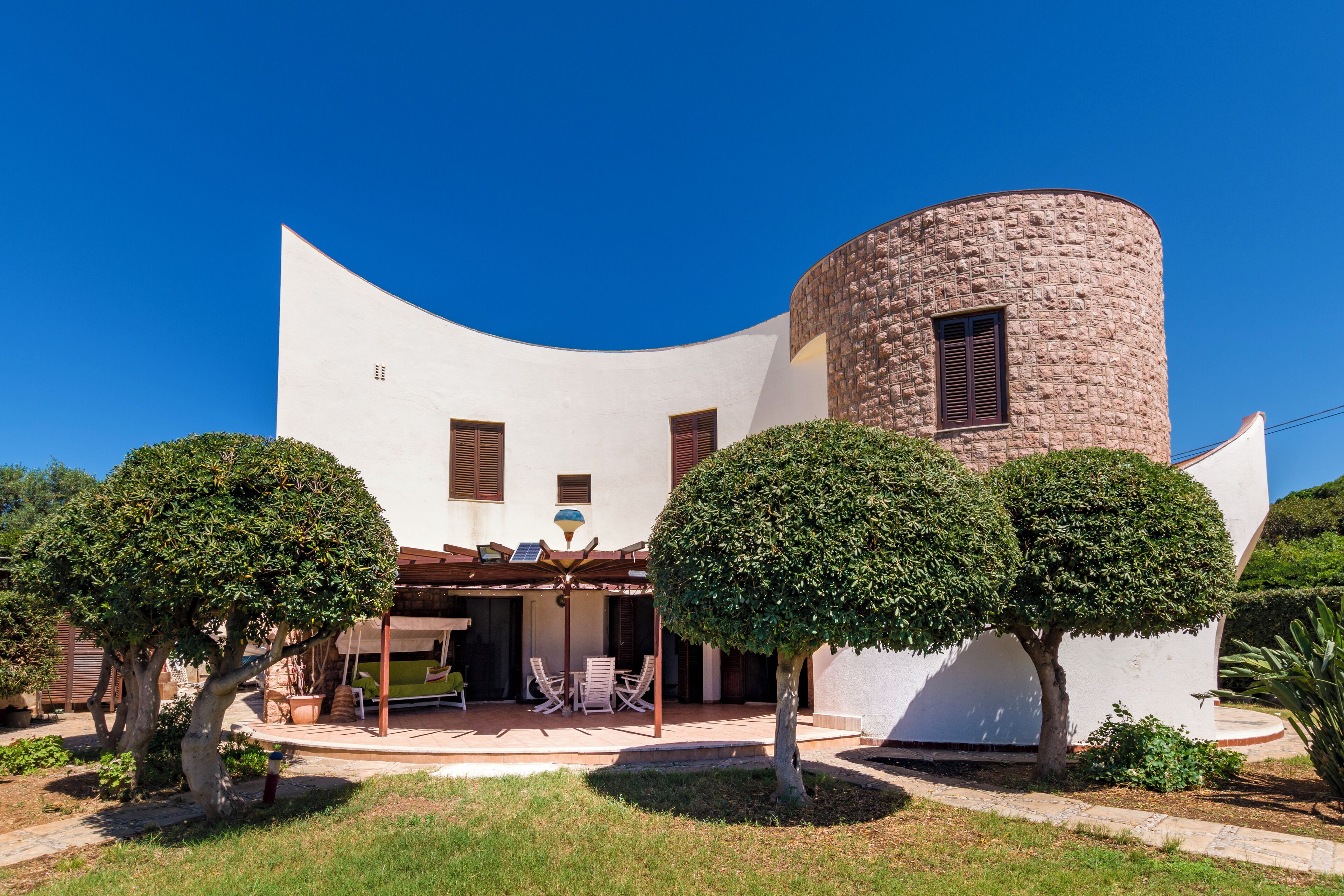 A modern house with a curved white facade, a stone tower, and a patio with outdoor furniture.