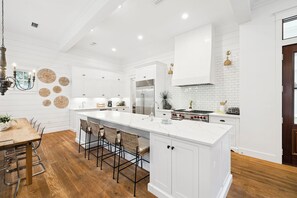 A modern kitchen with white cabinetry, a large island, and a dining area with wooden flooring and metal chairs. - Private Pool Retreat with 6-Passenger LSV, Fire Pit, and 5 Adult Bikes (Santa Rosa Beach)