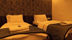 A hotel room with two beds, each with a headboard, and a wall with a geometric pattern. - The Flamboyant Natraj (Bharuch)