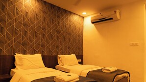A hotel room with two beds, a patterned wall, and an air conditioning unit. - The Flamboyant Natraj (Bharuch)