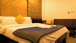 A hotel room with a large bed, a wooden headboard, a patterned wall, and a small table with a chair. - The Flamboyant Natraj (Bharuch)