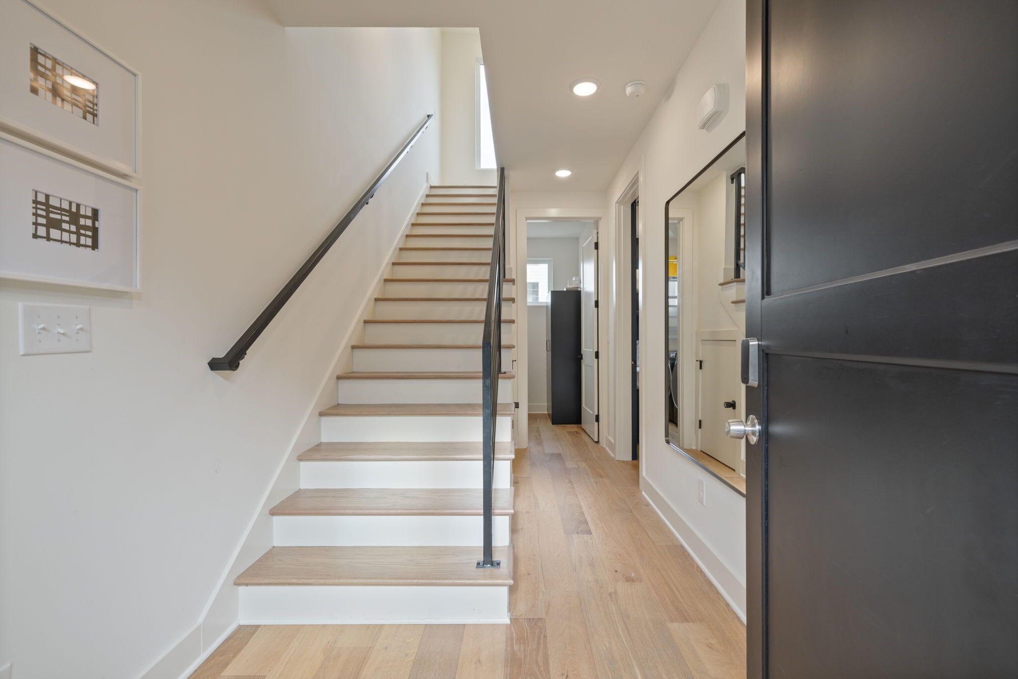 Un interior moderno con una escalera de madera, una zona de cocina y un pasillo que conduce a otra habitación.