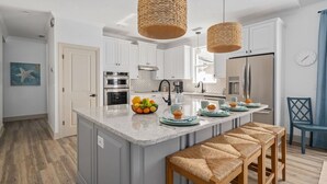Une cuisine moderne dotée d’un îlot central, de deux suspensions en osier et d’un banc en bois.
