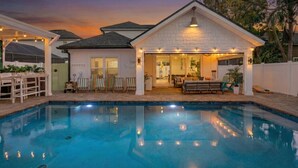 Une piscine avec une maison en arrière-plan, un patio avec des chaises et un espace extérieur aménagé avec un toit.