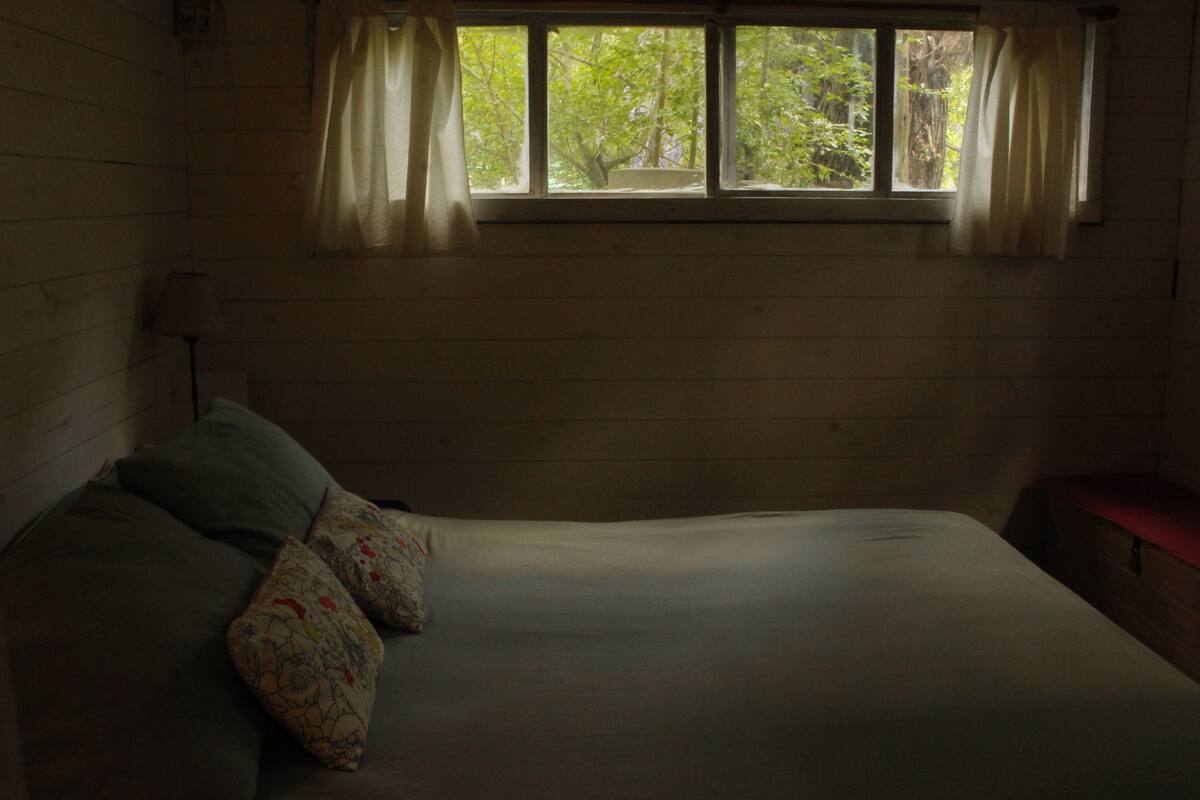 Een kamer met een bed, een raam met gordijnen en een houten wand.