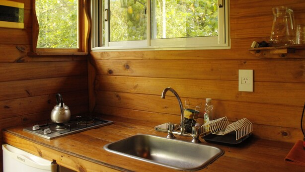 Eine Holzhütte mit Küche, inklusive Fenster, Spüle, Herd und Geschirrständer.