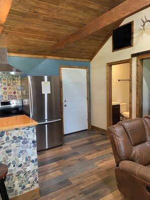 A kitchen with a stone backsplash, stainless steel appliances, and a wooden ceiling.