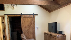 A cozy living area with a brown leather recliner, a wooden dining table, and a TV on a wooden cabinet. - Rustic Cabin Retreat Near the Nueces River (Camp Wood)