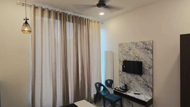 Una habitación de hotel moderna con una cama, un escritorio con una silla, un ventilador de techo y un gran ventanal con cortinas.
