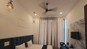 Habitación de hotel con cama, escritorio, silla, ventilador de techo y televisor montado en la pared.