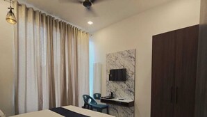 Una habitación de hotel moderna con una cama, un escritorio con televisor de pantalla plana, un armario y un ventilador de techo.