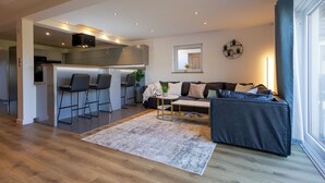 Un salon moderne avec un canapé, une table basse et un tapis. Il y a également un coin cuisine avec des tabourets de bar et une table à manger.