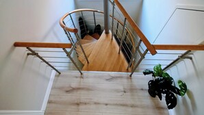Un escalier en bois avec une rampe métallique menant à une mezzanine dotée d’un puits de lumière.