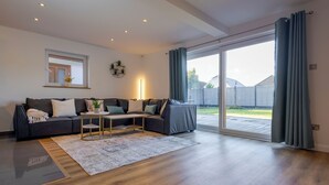 Un salon moderne avec un canapé d’angle gris foncé, une petite table basse en bois et une grande porte-fenêtre coulissante donnant sur un jardin.
