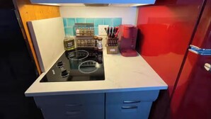Una cocina compacta con estufa negra, armarios azules y refrigerador rojo.