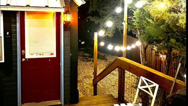 Una terraza de madera con una puerta roja y una silla blanca.