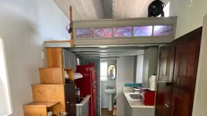 Un estrecho pasillo con escaleras de madera que conducen a una pequeña cocina, un lavabo y un espejo.