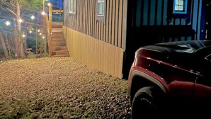 Una casa pequeña con fachada de madera, una escalera visible y un coche estacionado en frente.