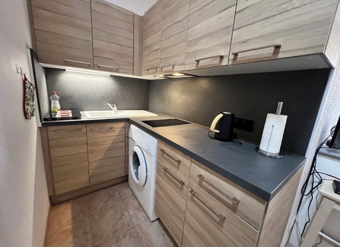 Een compacte keuken met houten kastjes, een wasmachine, een spoelbak en een koffiezetapparaat.