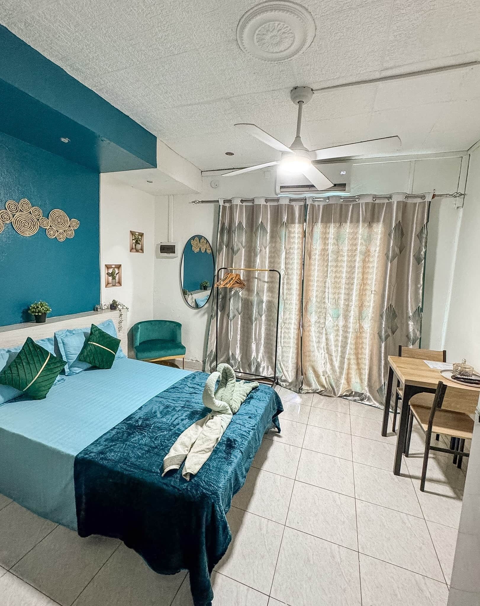 A hotel room with a bed, a desk, a chair, a ceiling fan, and a window with curtains.