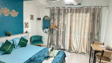 A hotel room with a bed, a desk, a chair, a ceiling fan, and a window with curtains.