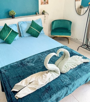 Ein Bett mit blauer Bettdecke und Kissen, ein türkisfarbenes Sessel und ein schwanenförmiges Handtuch auf dem Bett.
