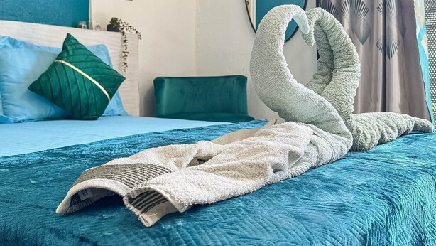A neatly made bed with a blue bedspread and a white blanket, a green pillow, and a decorative wall art piece.