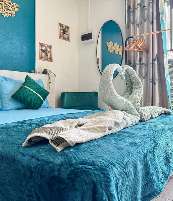 A neatly made bed with a blue bedspread and a white blanket, a green pillow, and a decorative wall art piece.