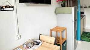 A compact kitchen with a TV mounted above a counter, a small wooden table with a plate and menu, and a sign indicating a WiFi code.
