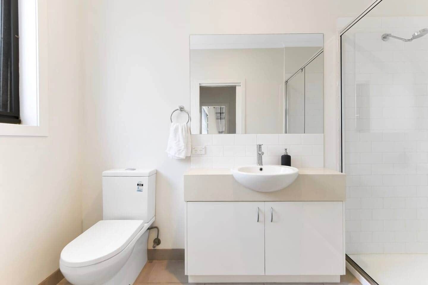 A modern bathroom with a toilet, sink, mirror, and shower.