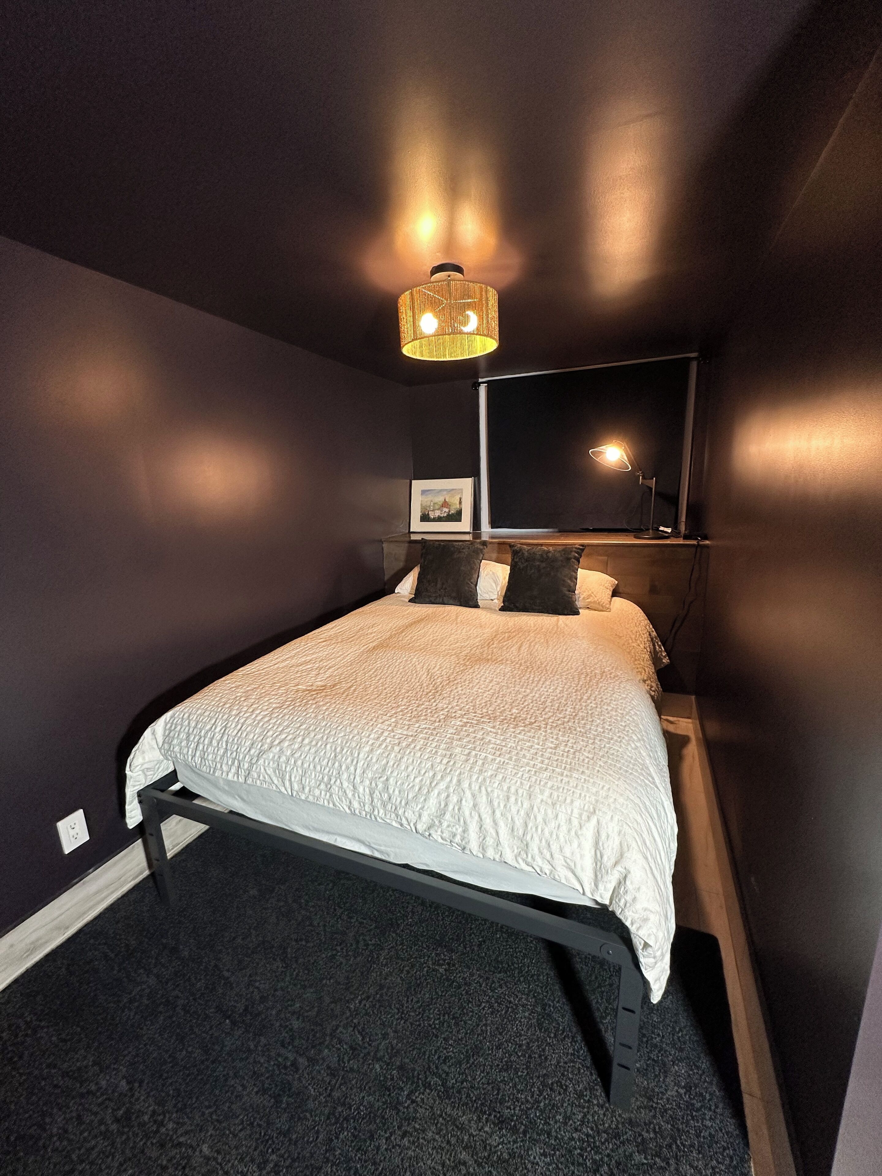 Ein Schlafzimmer mit Bett, Nachttischlampe, Wandspiegel und Deckenleuchte.
