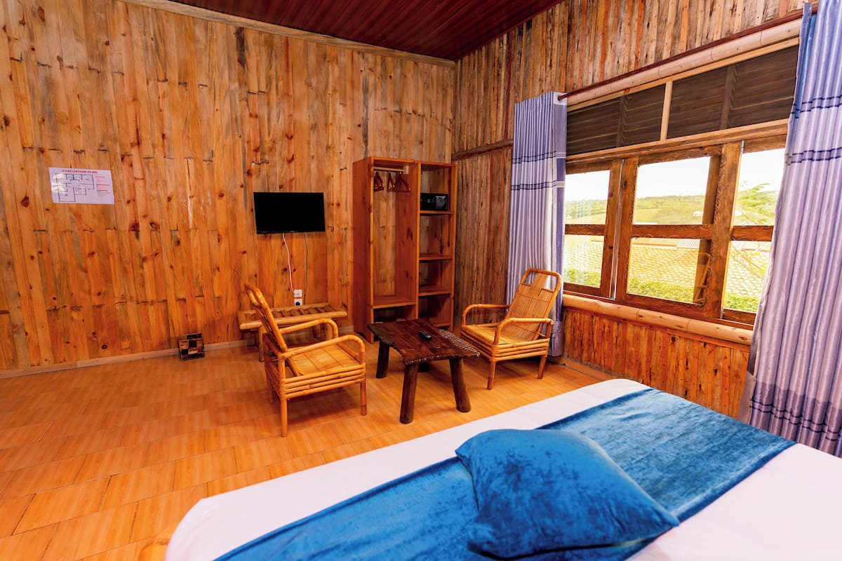 A wooden room with a bed, two chairs, a table, and a bookshelf.