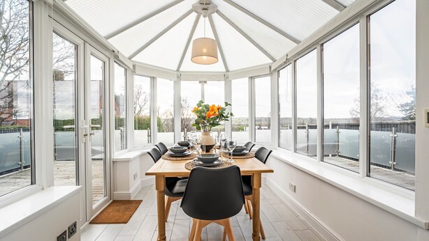 Une véranda avec une table à manger dressée pour six personnes, entourée de grandes fenêtres.