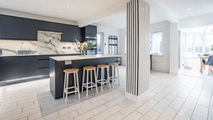 Une cuisine moderne dotée d’un plan de travail en marbre, de meubles de rangement aux couleurs sombres et d’un îlot central avec des tabourets de bar.
