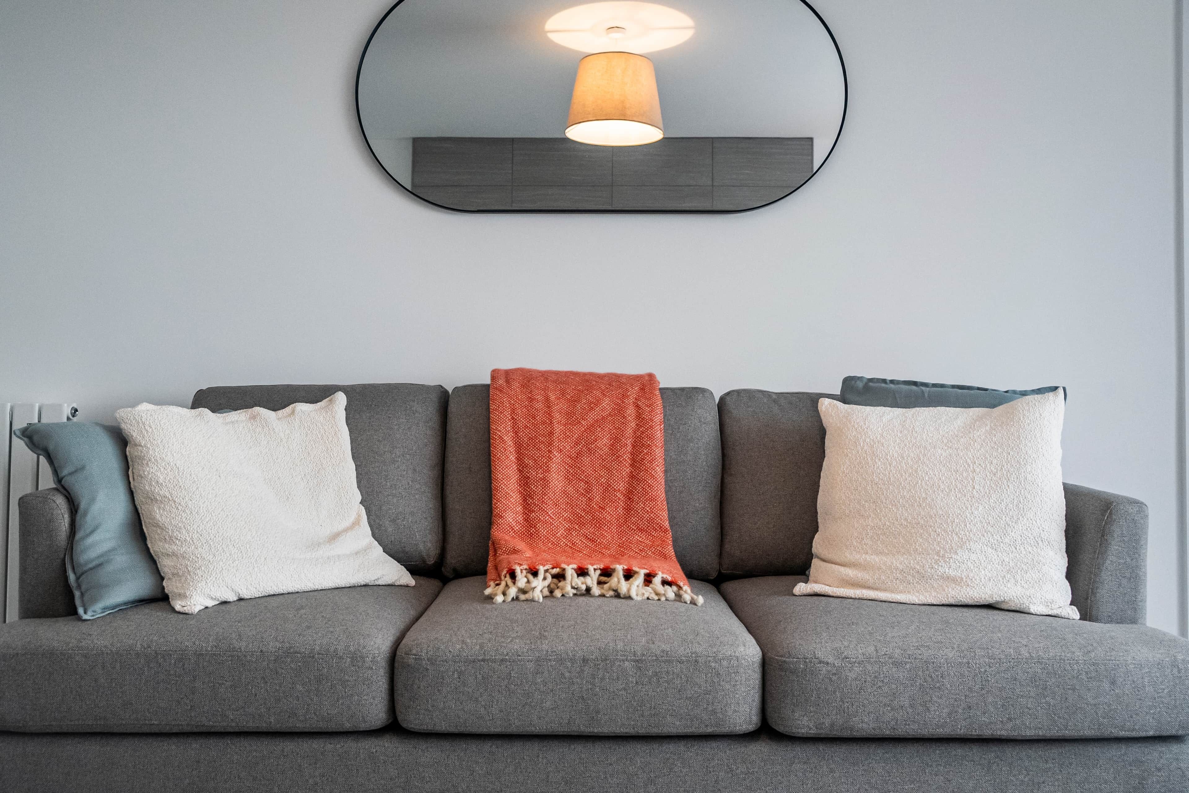 A grey sofa with three pillows and a red throw blanket.