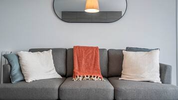 A grey sofa with three pillows and a red throw blanket.