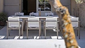 En bygning med en terrasse, udendørs møbler og et træ i forgrunden.